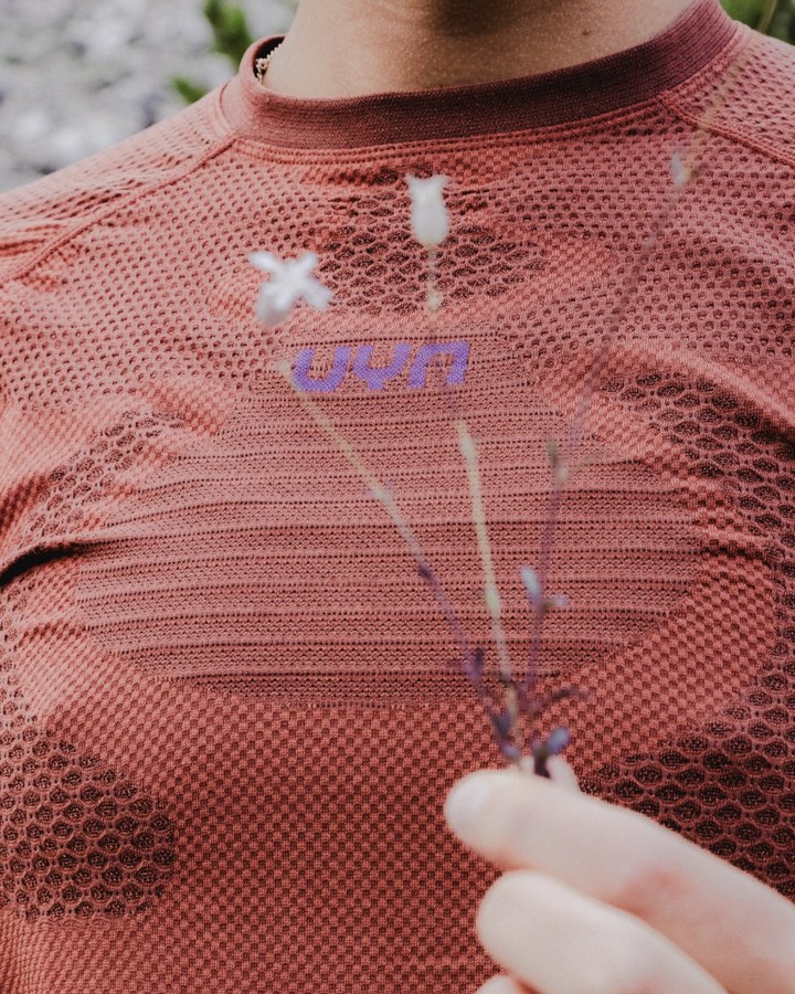 Maglia sportiva UYN con logo, tra le mani un ramo di fiori selvatici